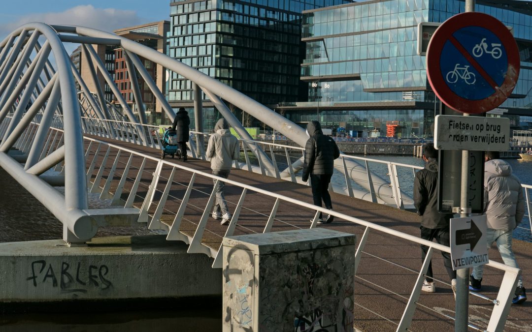 Young Dutch people walking on a modern bridge with a 'no cycling' sign and urban buildings in the background.