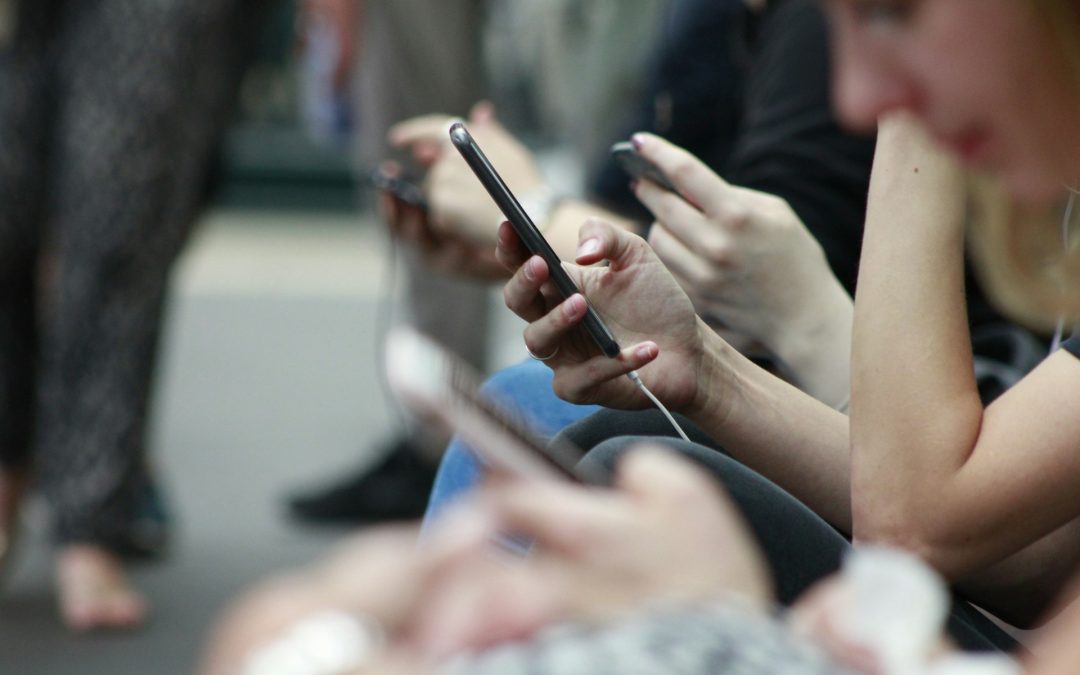 Italian young people looking at their phones, seated in a row, with a focus on their hands and devices.