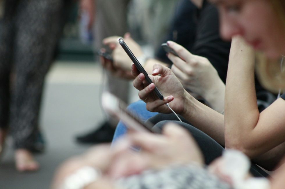 Italian young people looking at their phones, seated in a row, with a focus on their hands and devices.